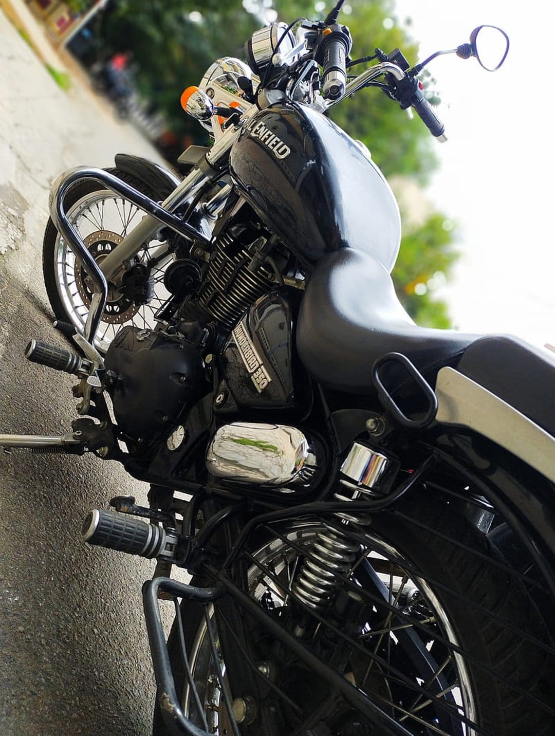 Black Royal Enfield motorcycle shows polished chrome handlebars and mirrors against a blurred outdoor background.