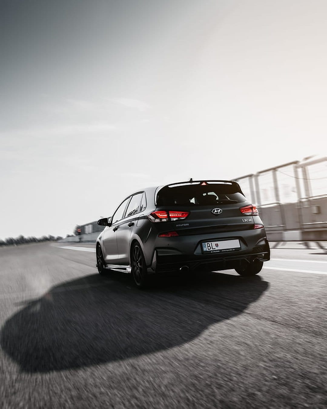 Hyundai i30 N Fastback rear view with glowing taillights and motion blur on a dark grey asphalt race track.