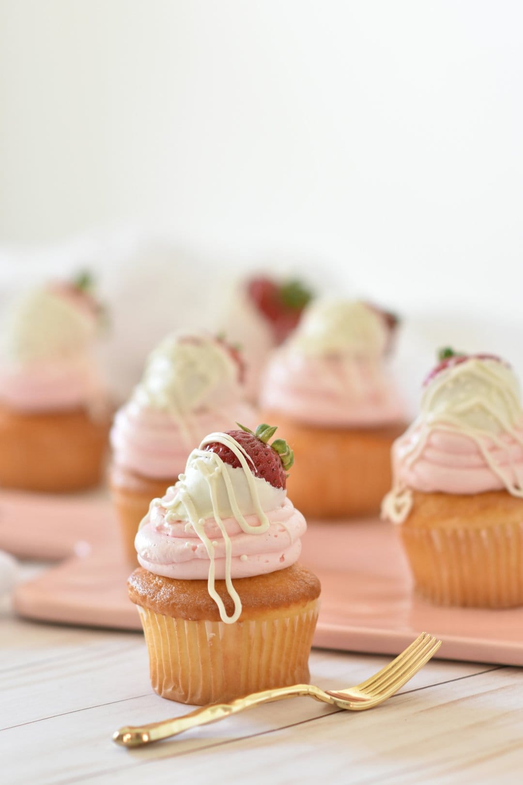 Strawberry cupcakes with swirled pink frosting, white chocolate drizzle, and fresh fruit garnish in close-up.