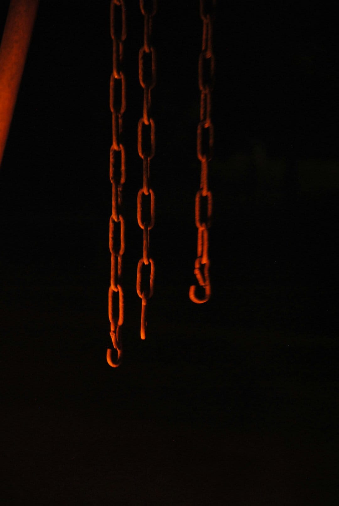 Three metallic chains illuminated with orange light against a solid black background show detailed iron links.