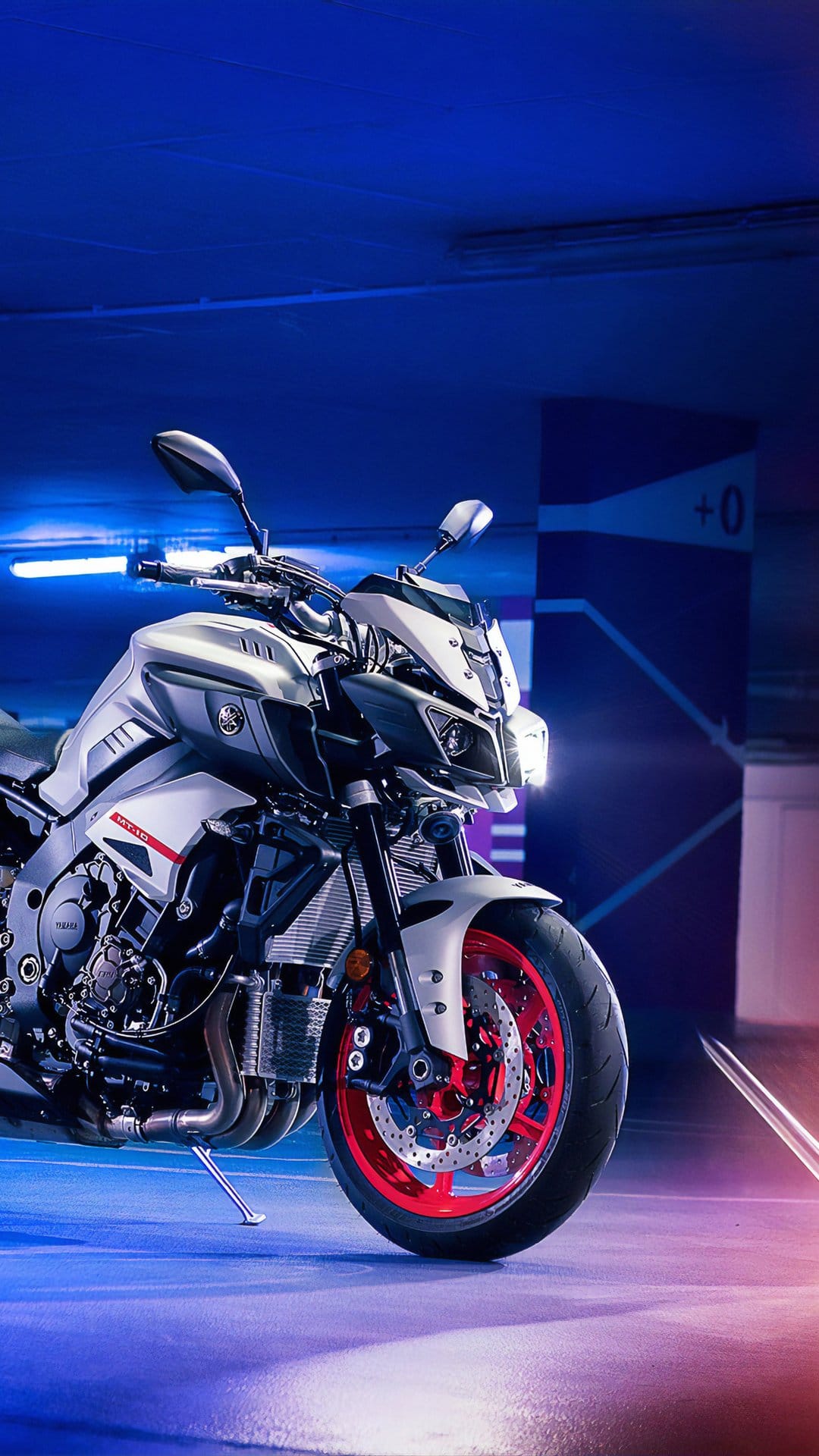 Yamaha naked motorcycle with red wheels glows under purple and blue neon lights on a reflective studio floor.