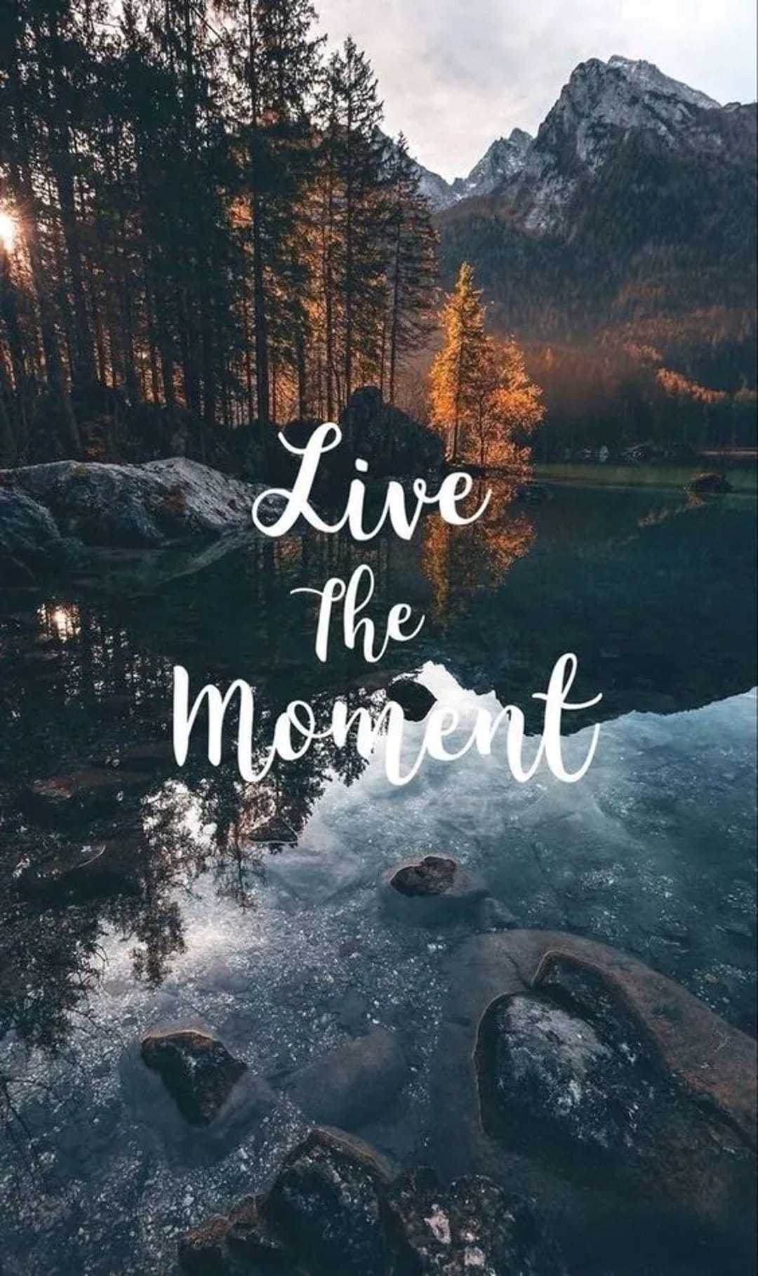 Live the Moment quote centered over a calm mountain lake reflection with snowy peaks and a clear blue sky.