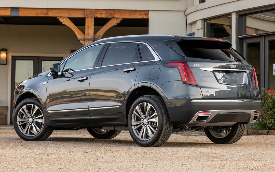 Dark gray Cadillac XT5 SUV rear profile parked on gravel in front of a modern building with wooden beams.