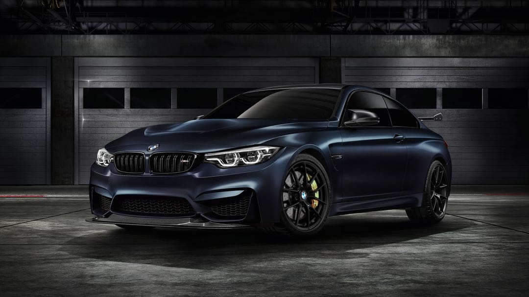 Matte navy BMW M4 GTS sports car in a dark industrial garage with dramatic lighting and gold brake calipers.