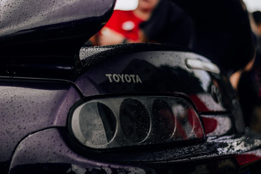 Purple Toyota Supra rear taillights and wing spoiler glistening with rain droplets during a moody night.