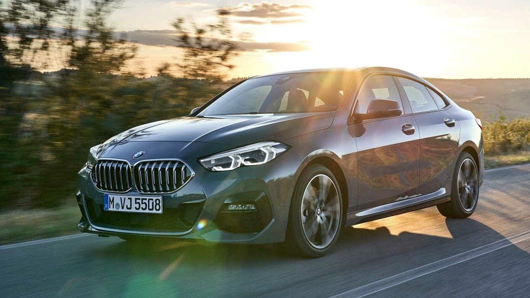Grey BMW luxury sedan driving on a scenic road at sunset with warm lens flare and motion blurred background.
