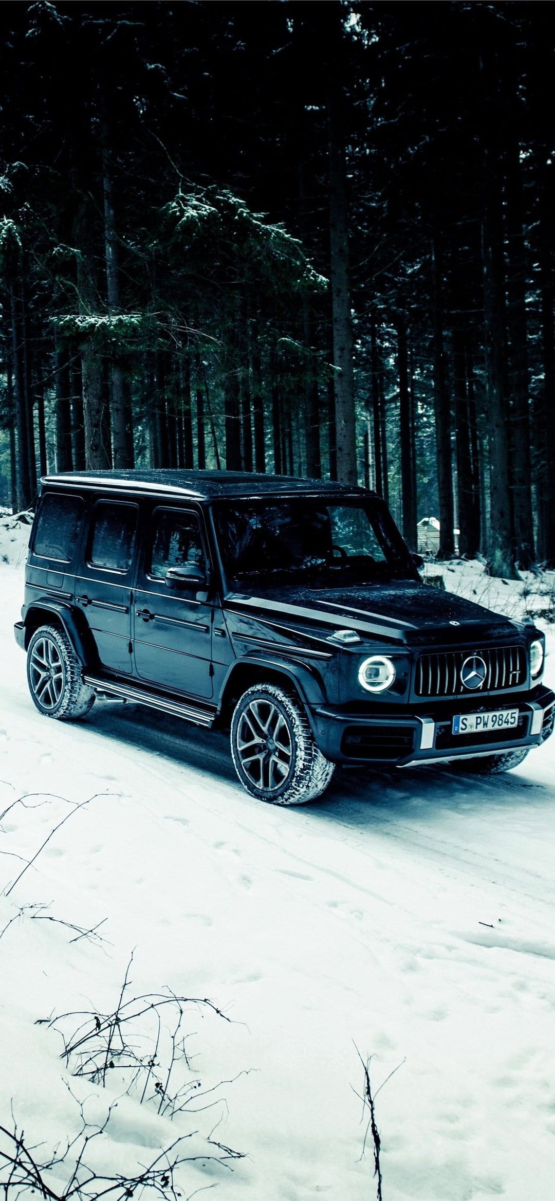 Black luxury SUV parked on a snowy trail surrounded by dark pine trees with glowing circular headlights.