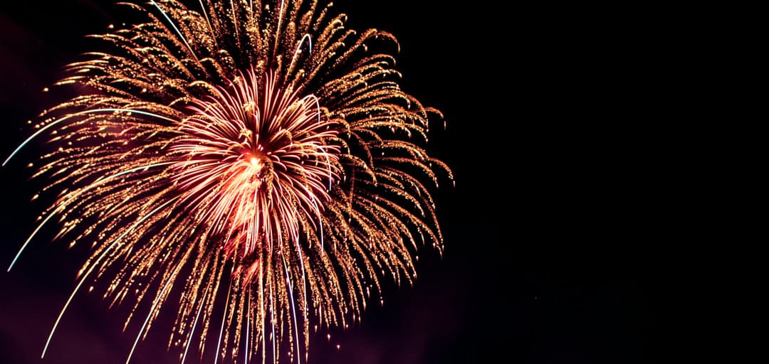 Golden and red fireworks explode in a radial pattern against a dark night sky during a celebratory event.
