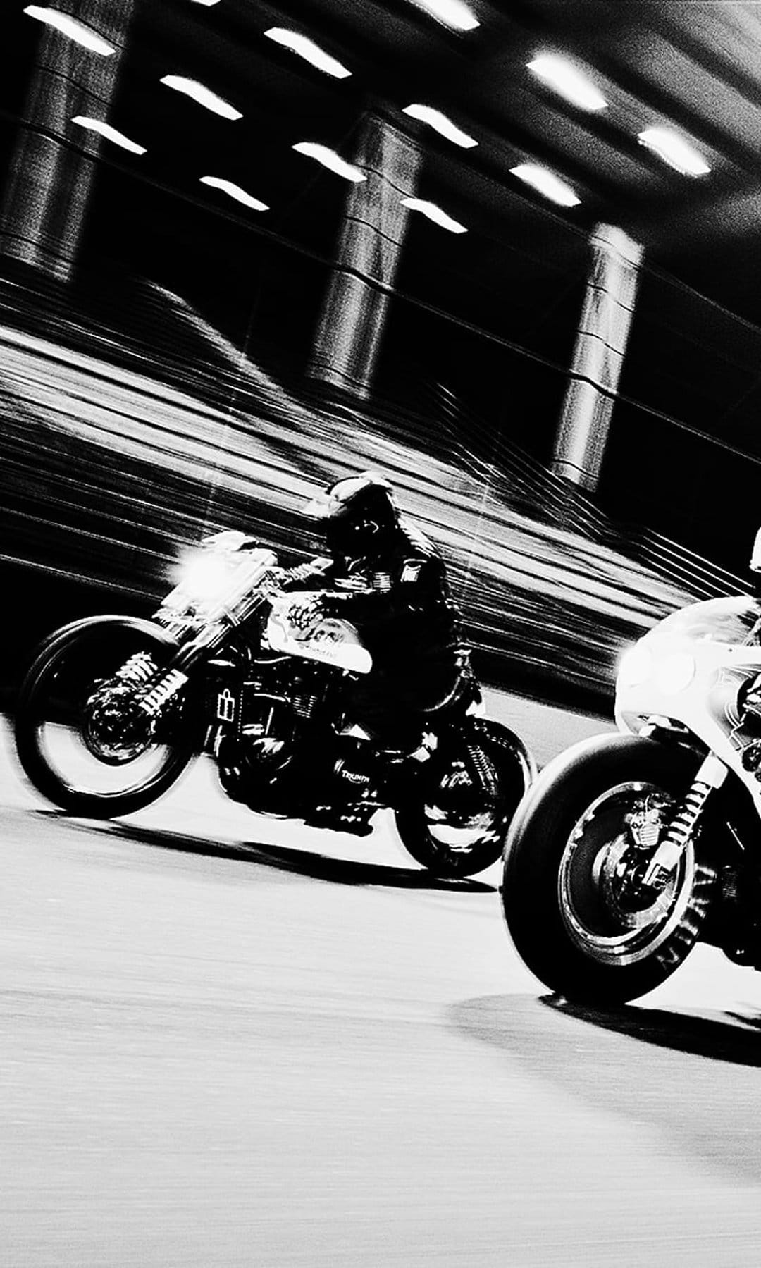 Motorcycle racer leaning into a curve with intense motion blur streaks in a high-contrast black and white style.