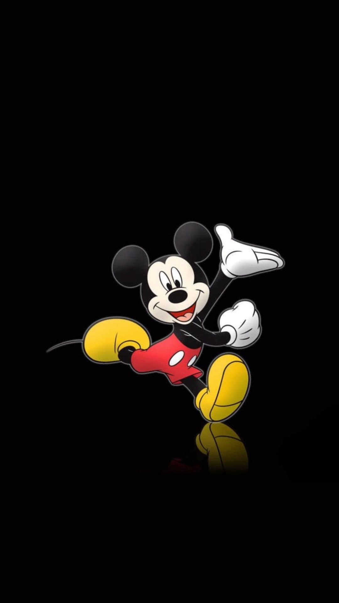 Mickey Mouse dances with one arm raised wearing red shorts and yellow shoes on a solid black background.