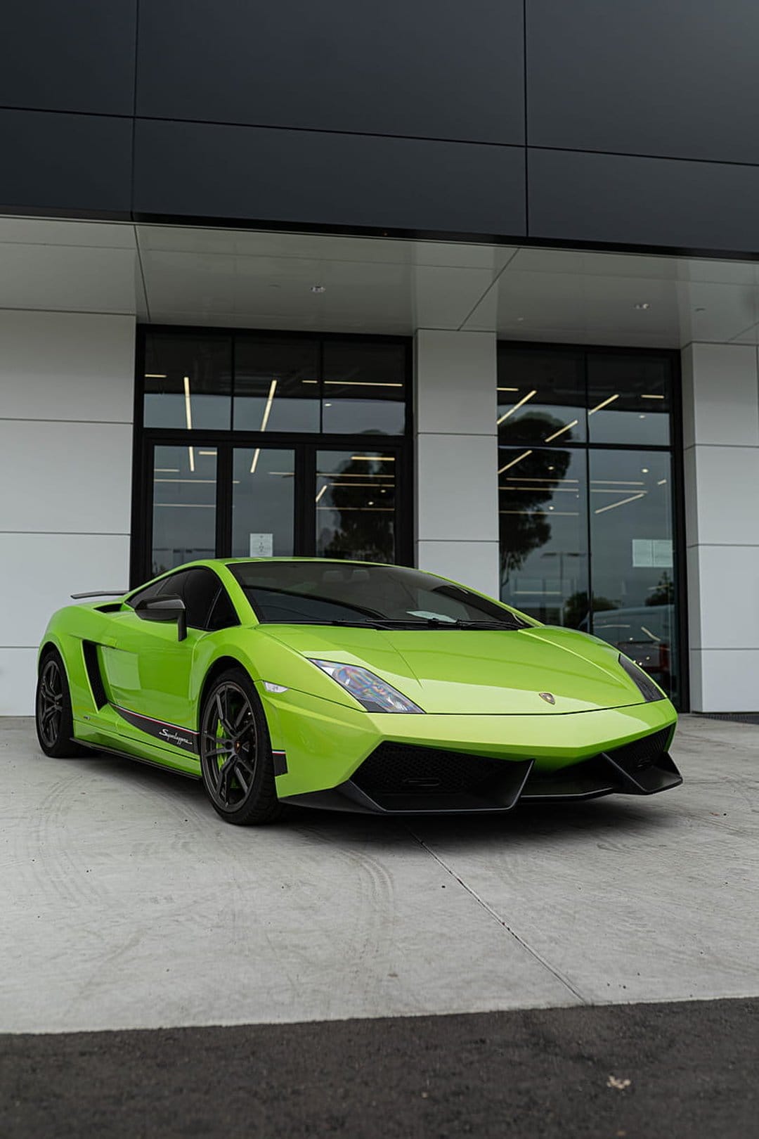 Neon green Lamborghini Gallardo Super Trofeo Stradale parked near a modern glass building in portrait view.