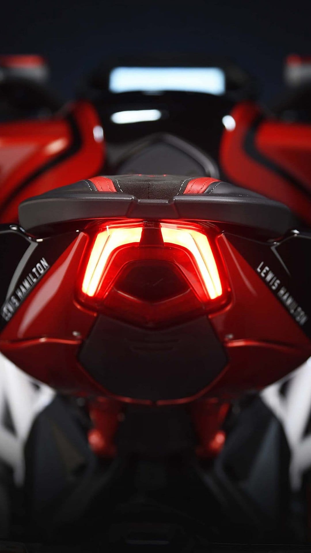 Red LED motorcycle tail light and Lewis Hamilton lettering on a sleek sportbike rear fairing against a black void.