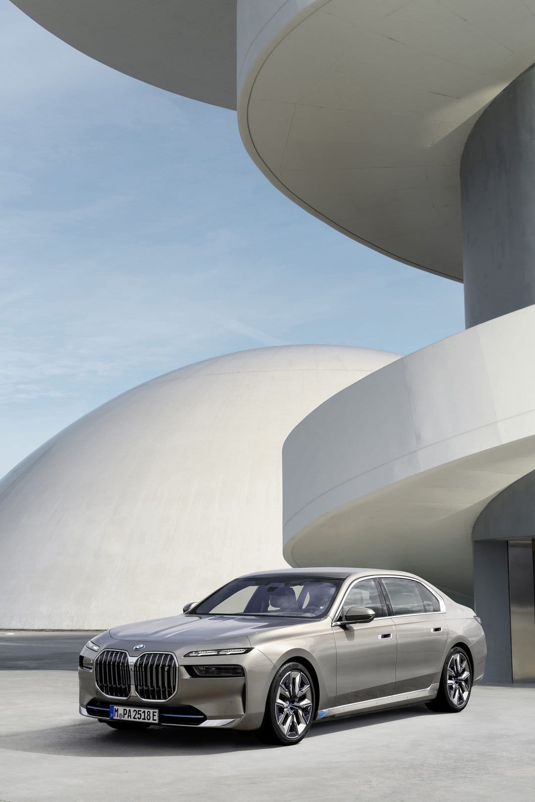 Silver BMW i7 luxury electric sedan parked beside curved white concrete walls and a large dome under a blue sky.