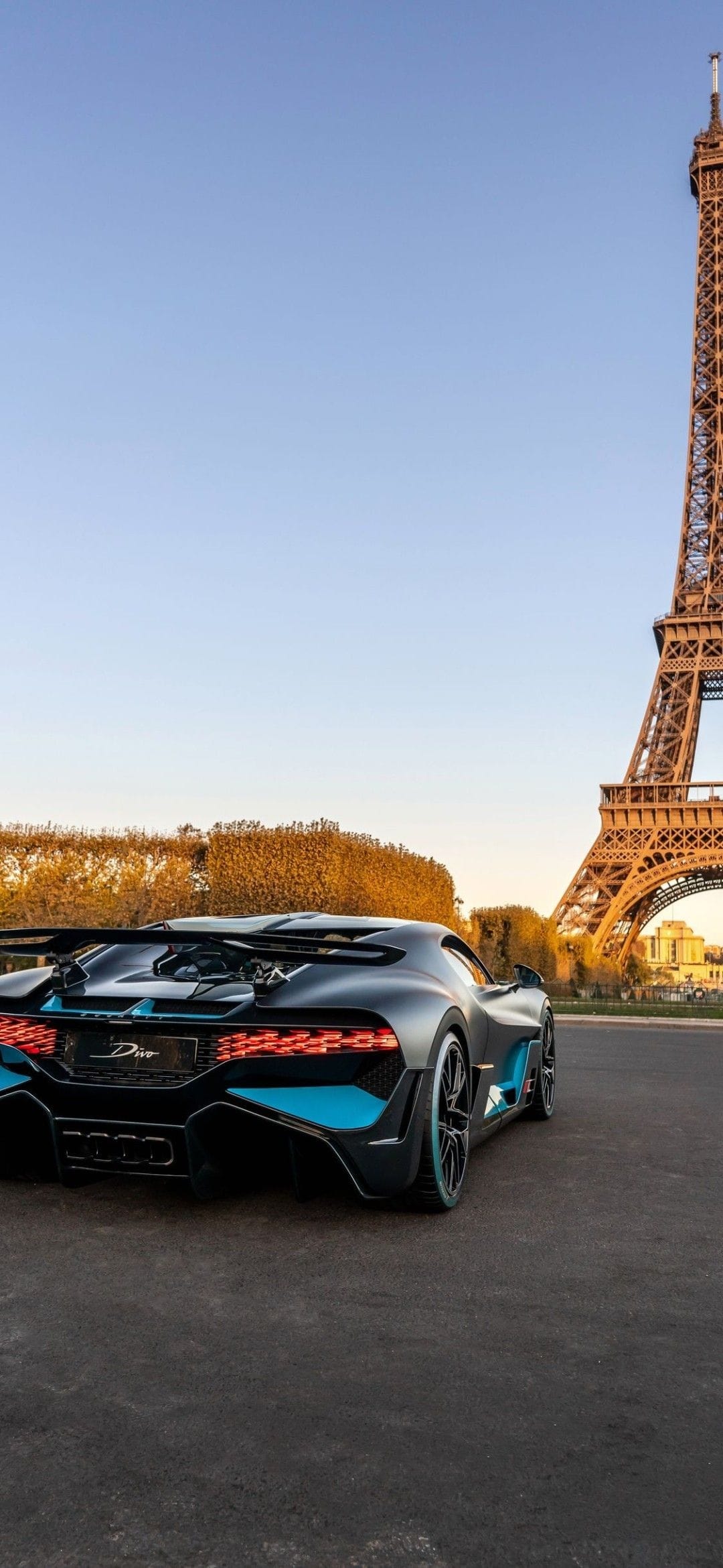 Matte grey Bugatti Divo with blue accents parked near the Eiffel Tower in Paris under a clear blue sky.