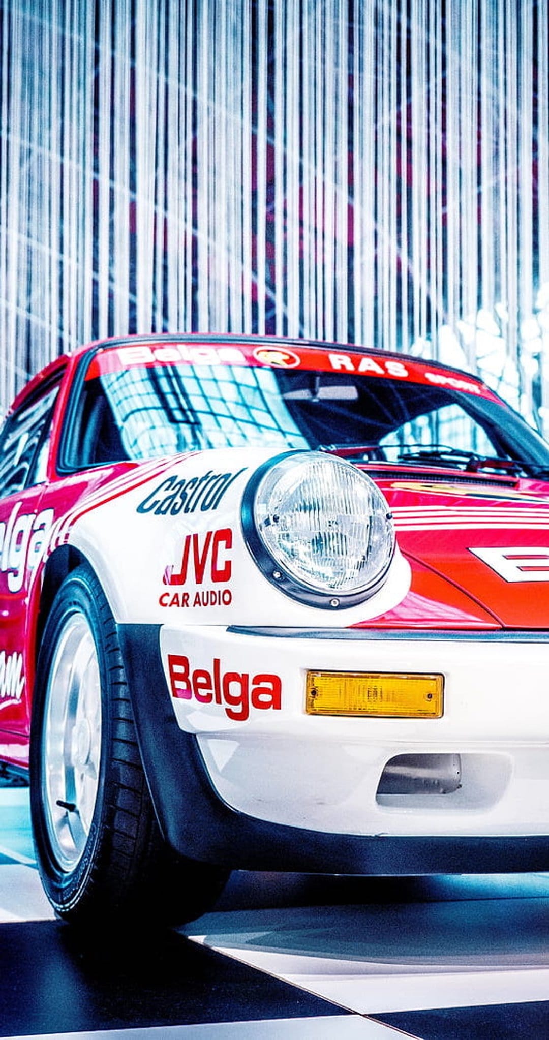 Porsche 911 race car featuring red and white Castrol livery, a round headlight, and wide tires on a dark track.
