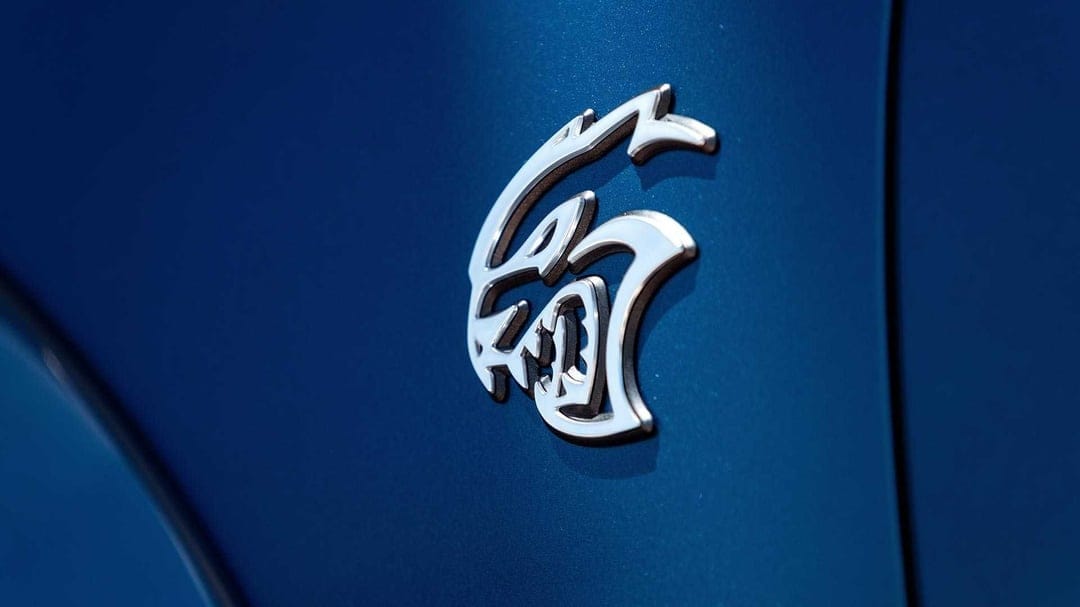 Chrome Hellcat emblem on a deep metallic blue car fender with sharp reflections and smooth paint texture.