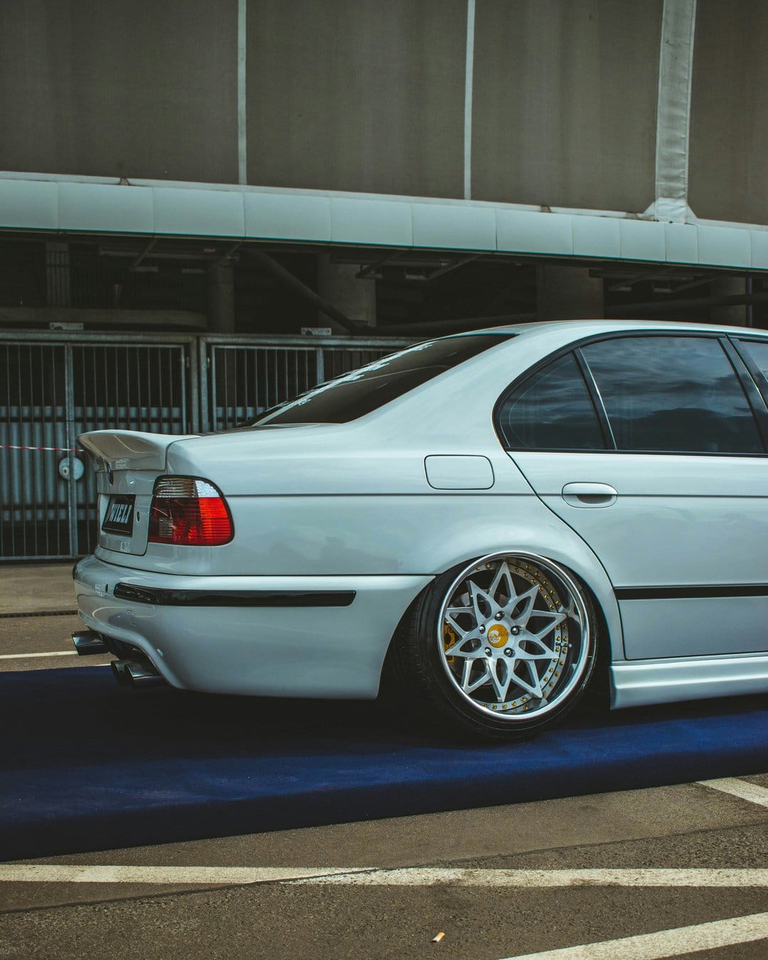 White BMW E39 M5 sedan with deep-dish chrome wheels and a slammed stance on a blue industrial studio floor.
