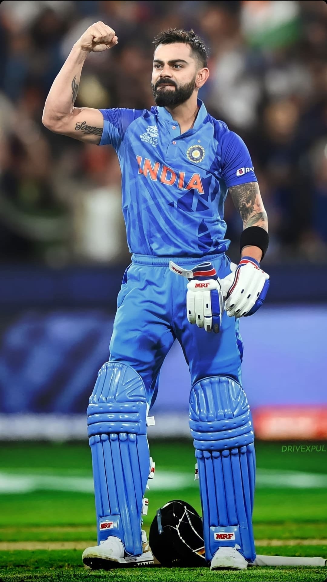 Virat Kohli celebrates victory in a blue India jersey and cricket helmet with a triumphant raised fist on field.