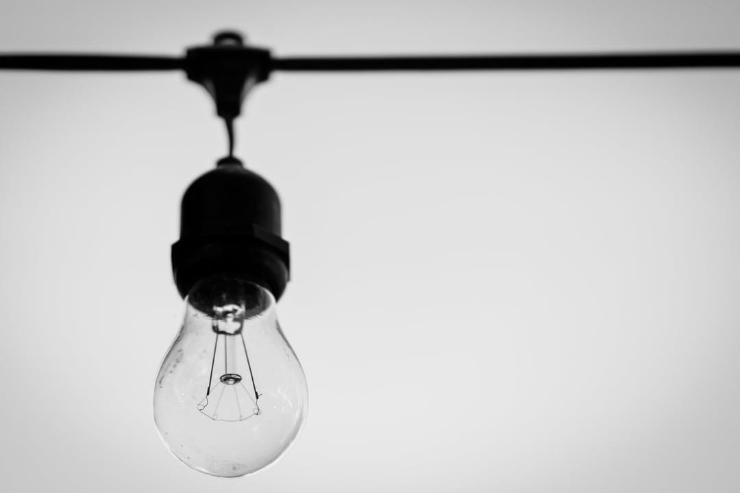 Incandescent light bulb with a glowing filament hangs from a black wire against a bright white background.