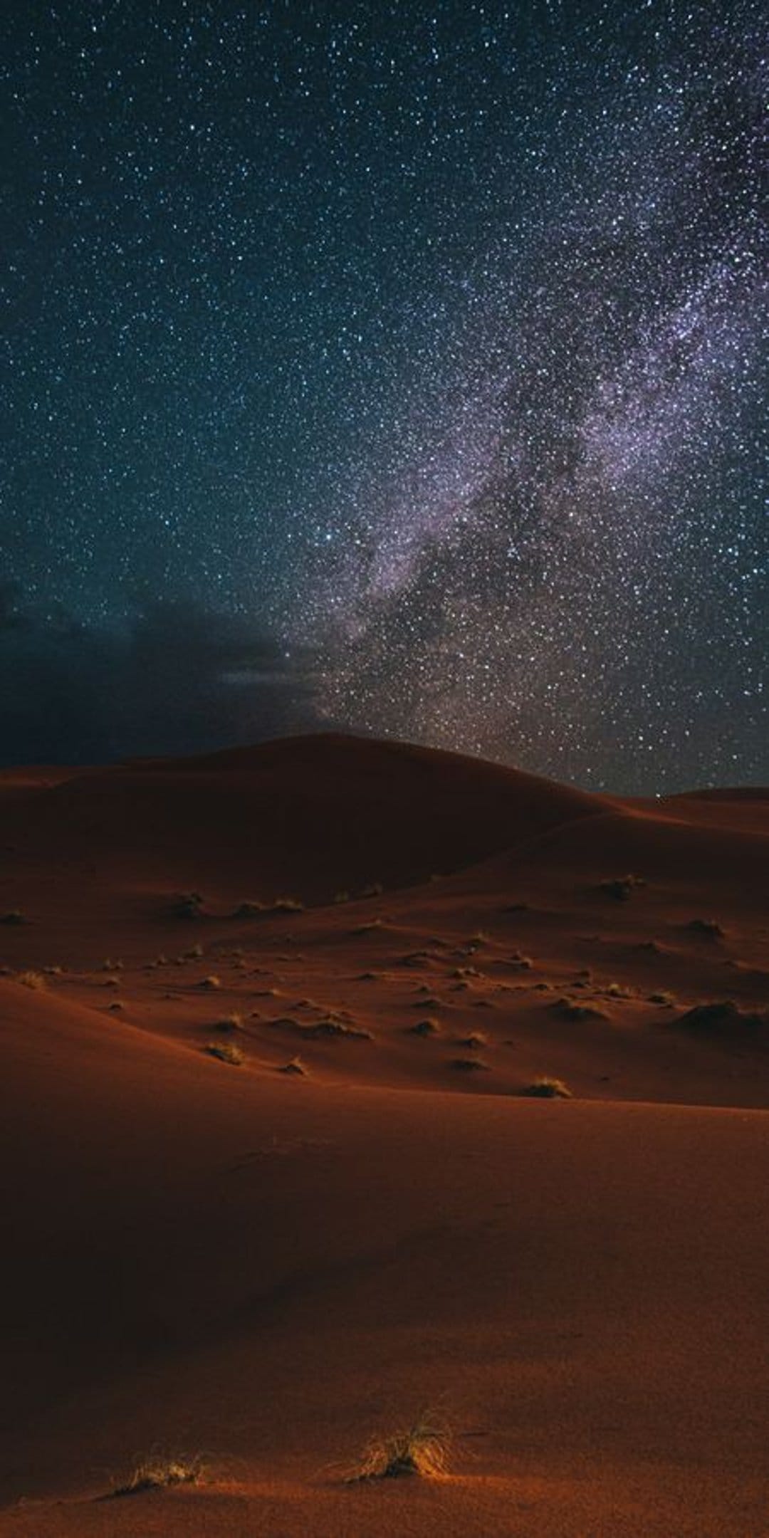 Rolling sand dunes under a bright Milky Way galaxy with dark clouds on the horizon and millions of visible stars.