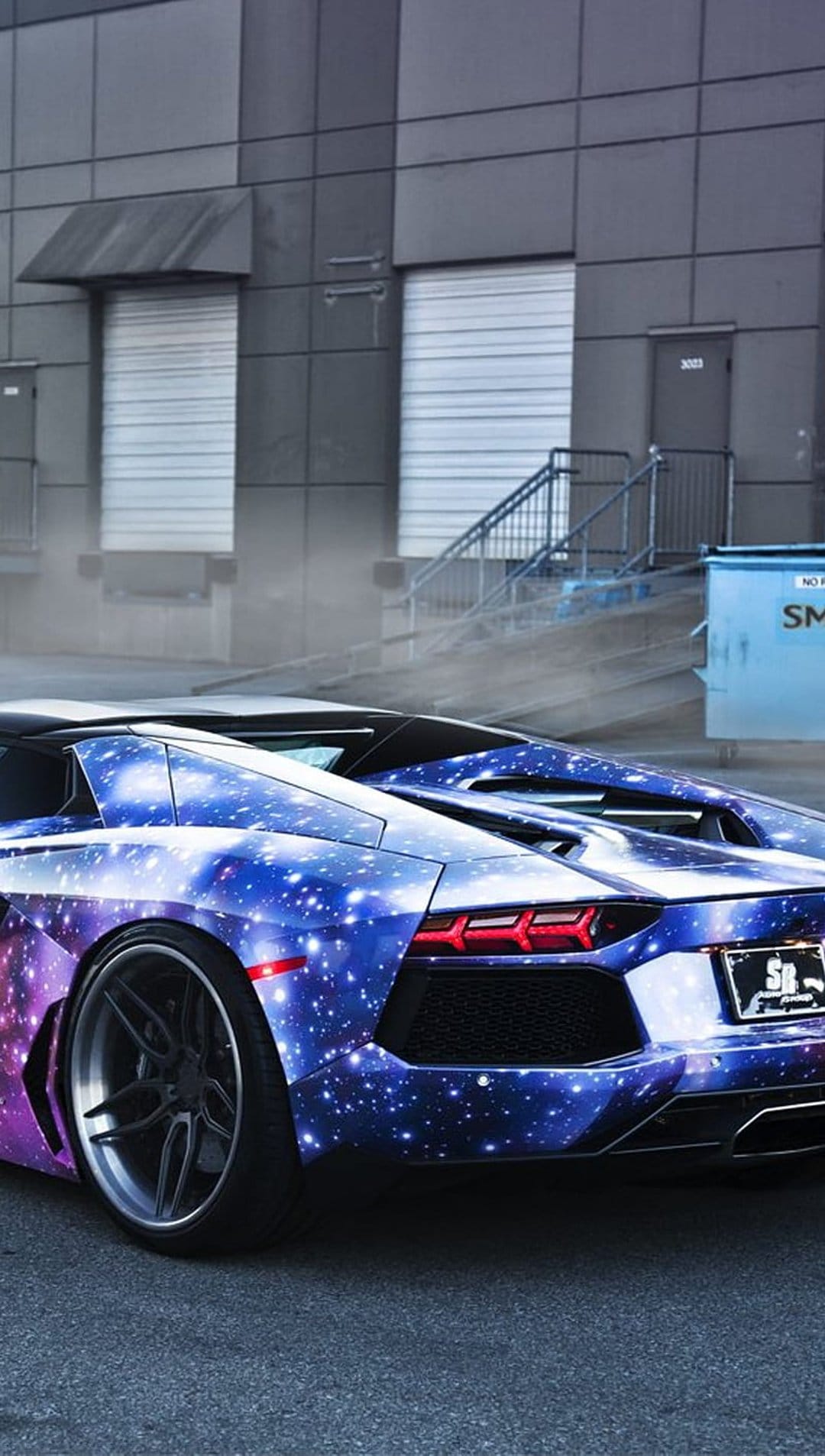 Lamborghini Aventador with blue and purple galaxy wrap parked beside an industrial building with metal stairs.