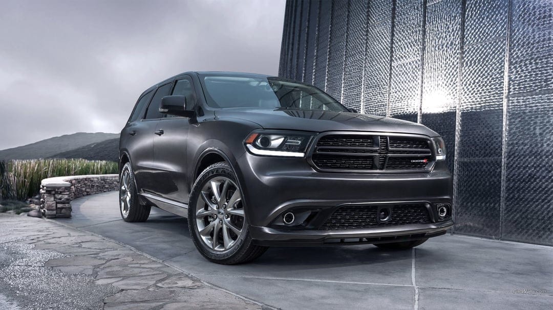 Charcoal Dodge Durango SUV parked on a stone walkway in front of a textured glass building under a cloudy sky.