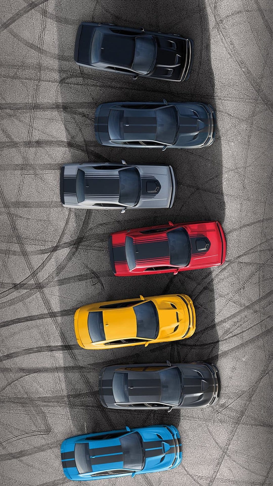 Eight muscle cars in diverse colors like red, yellow, and blue parked in a row on a dark asphalt racing track.