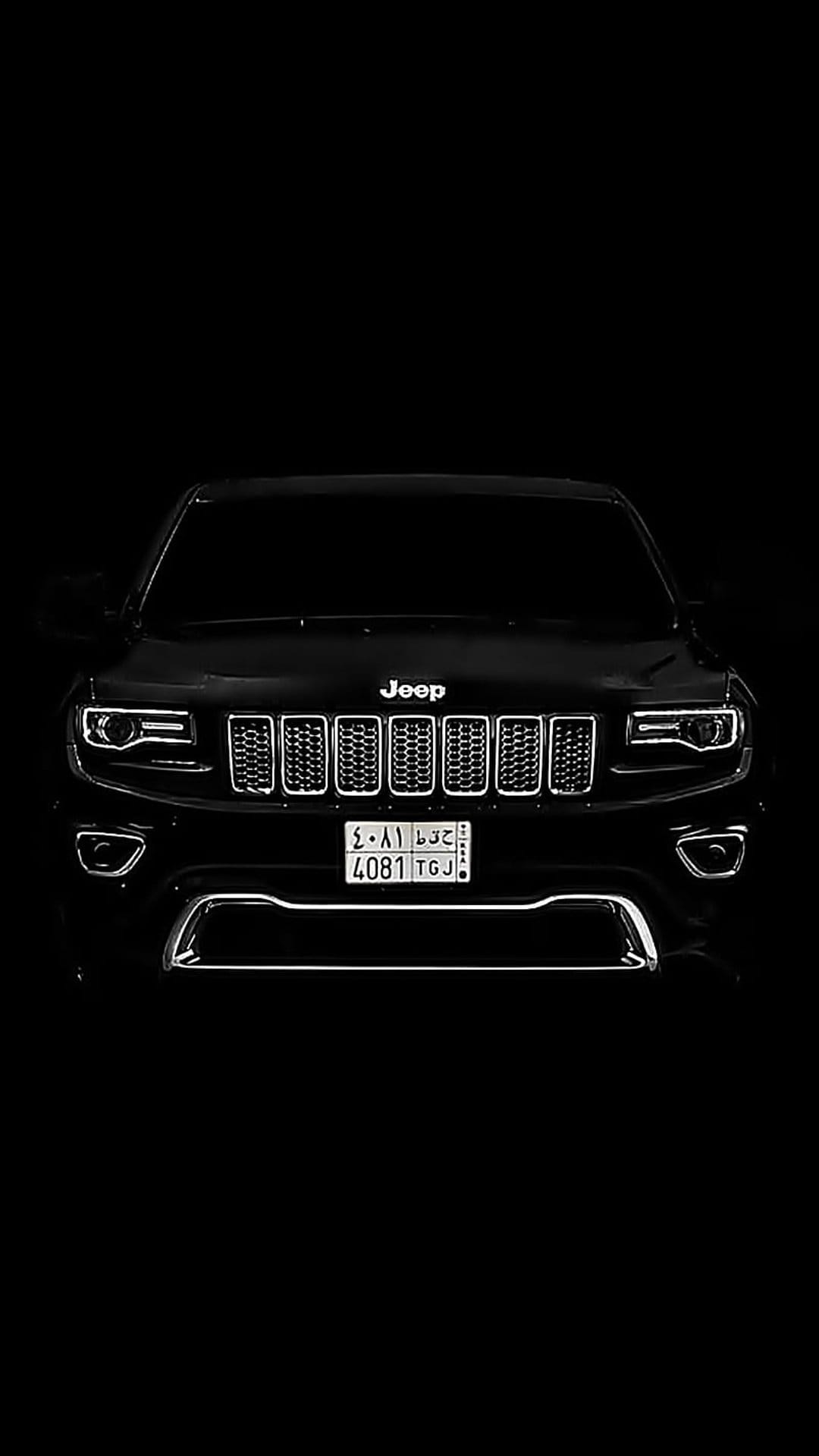 Black Jeep Grand Cherokee front view showing illuminated LED headlights and iconic grille against a dark background.