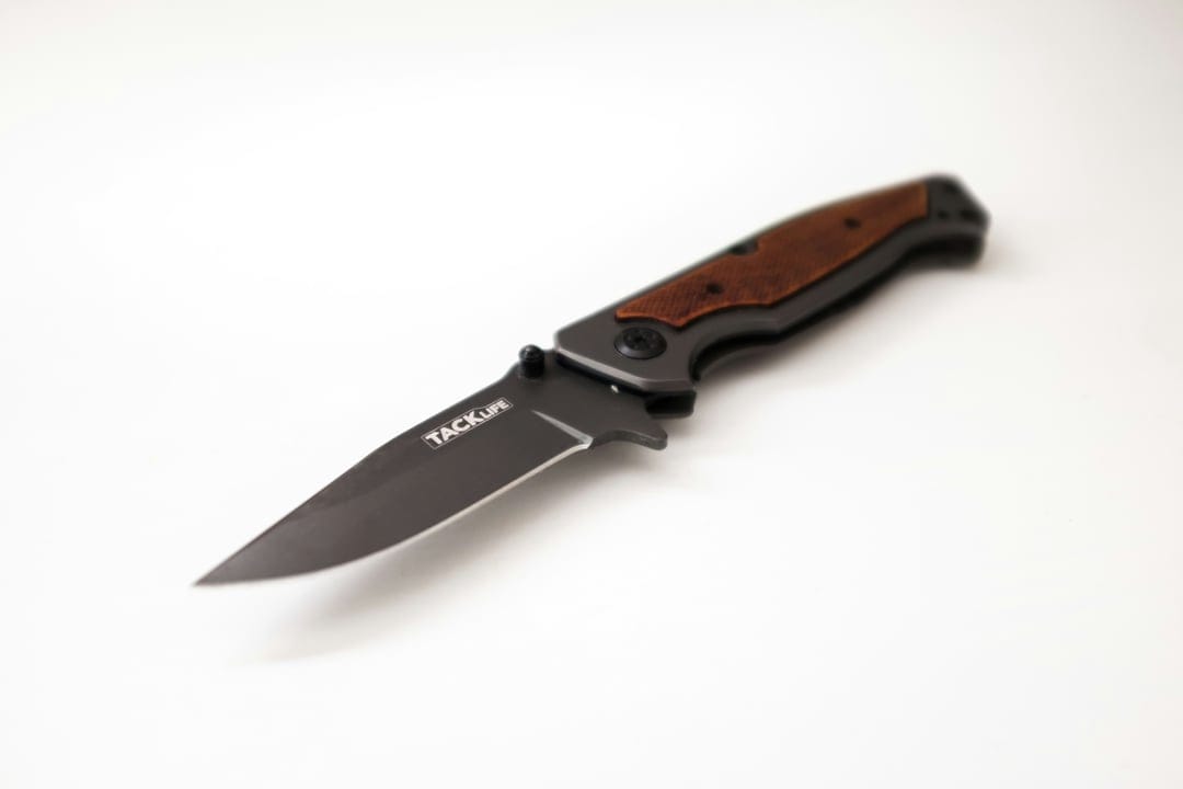Tactical folding knife with a black blade and wood handle inlay sits centered on a plain white background.