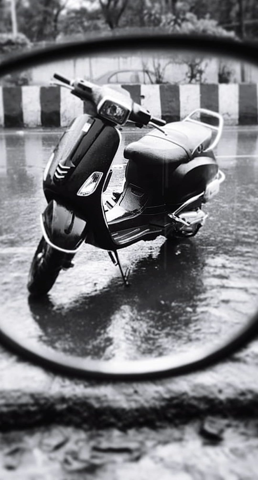 Vintage moped parked on a wet street reflects in a rain puddle with a circular bokeh blur and urban background.