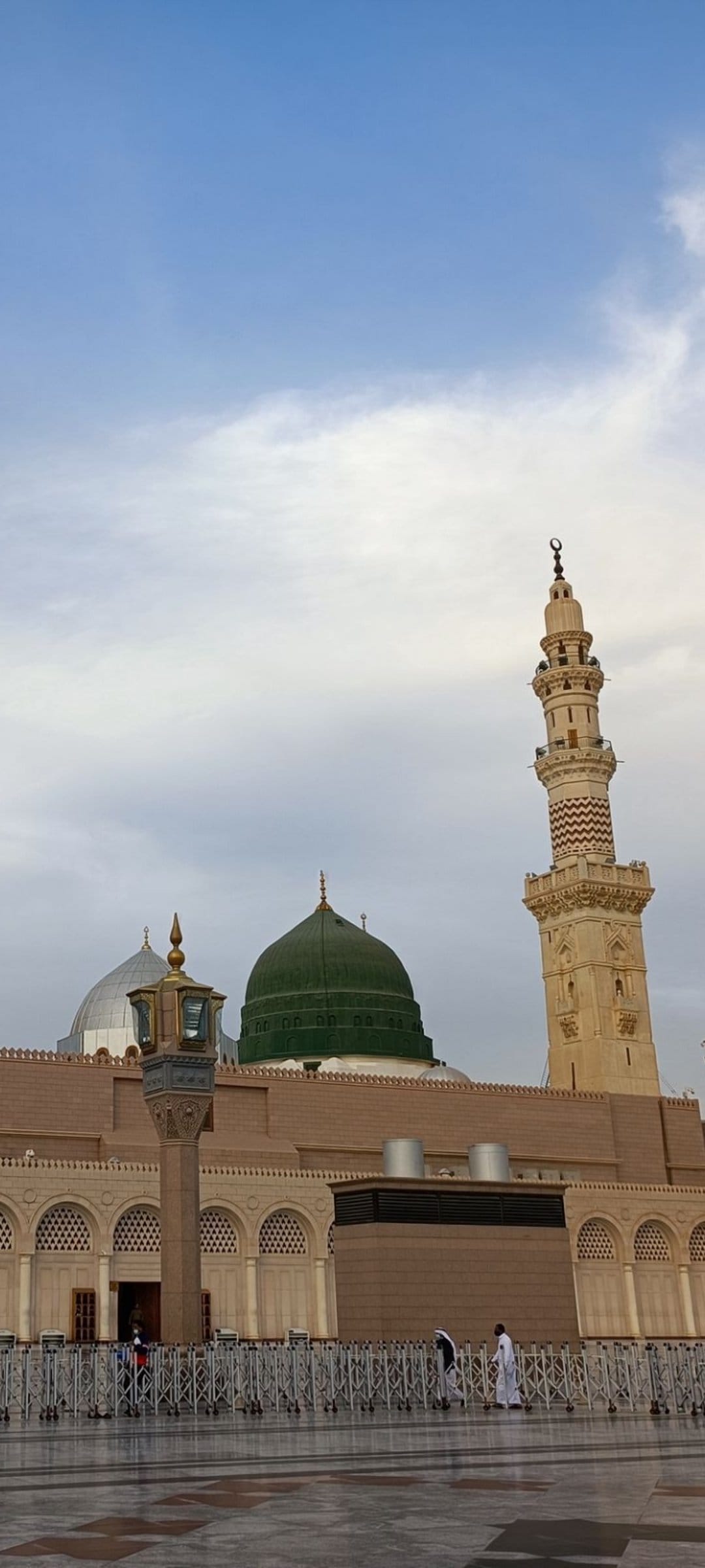 Green Dome of the Prophet's Mosque and a tall minaret under a blue sky with soft clouds in Medina, Saudi Arabia.