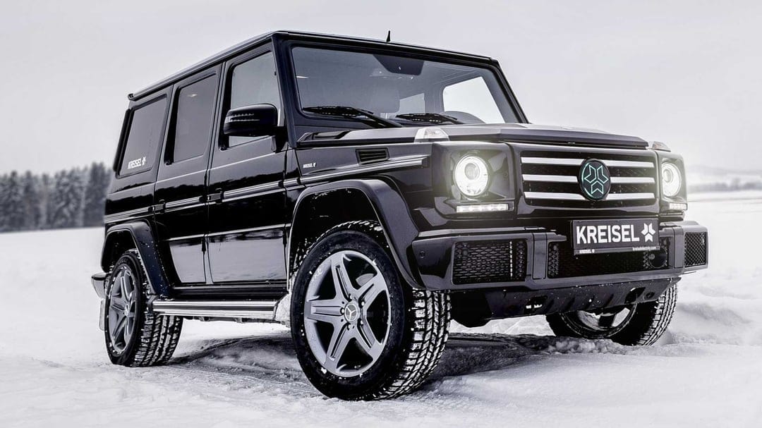 Black Mercedes-Benz G-Class electric SUV parked in a white snowy field with LED headlights illuminated.