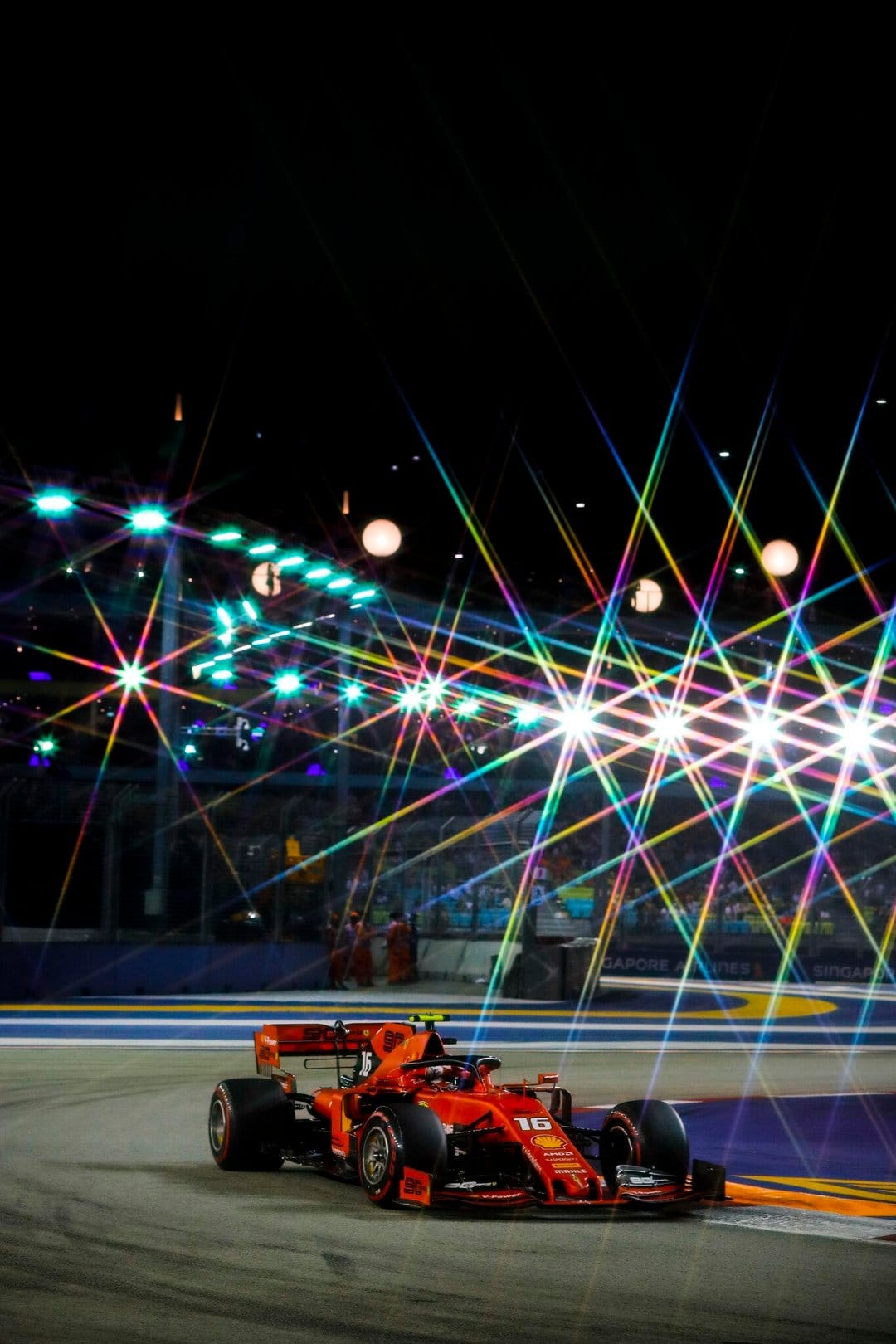 Red Ferrari Formula 1 car racing on a dark track under prismatic starburst lights and bright track lamps.