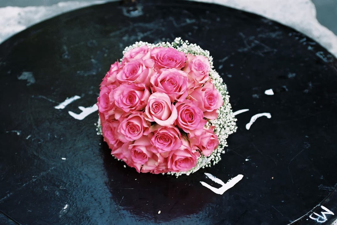 Pink rose bouquet with white baby's breath rests on a dark textured stone surface under soft lighting.
