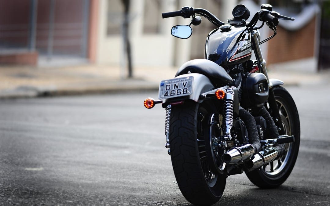 Rear view of a black Harley-Davidson cruiser motorcycle with chrome exhausts and red tail lights on a street.
