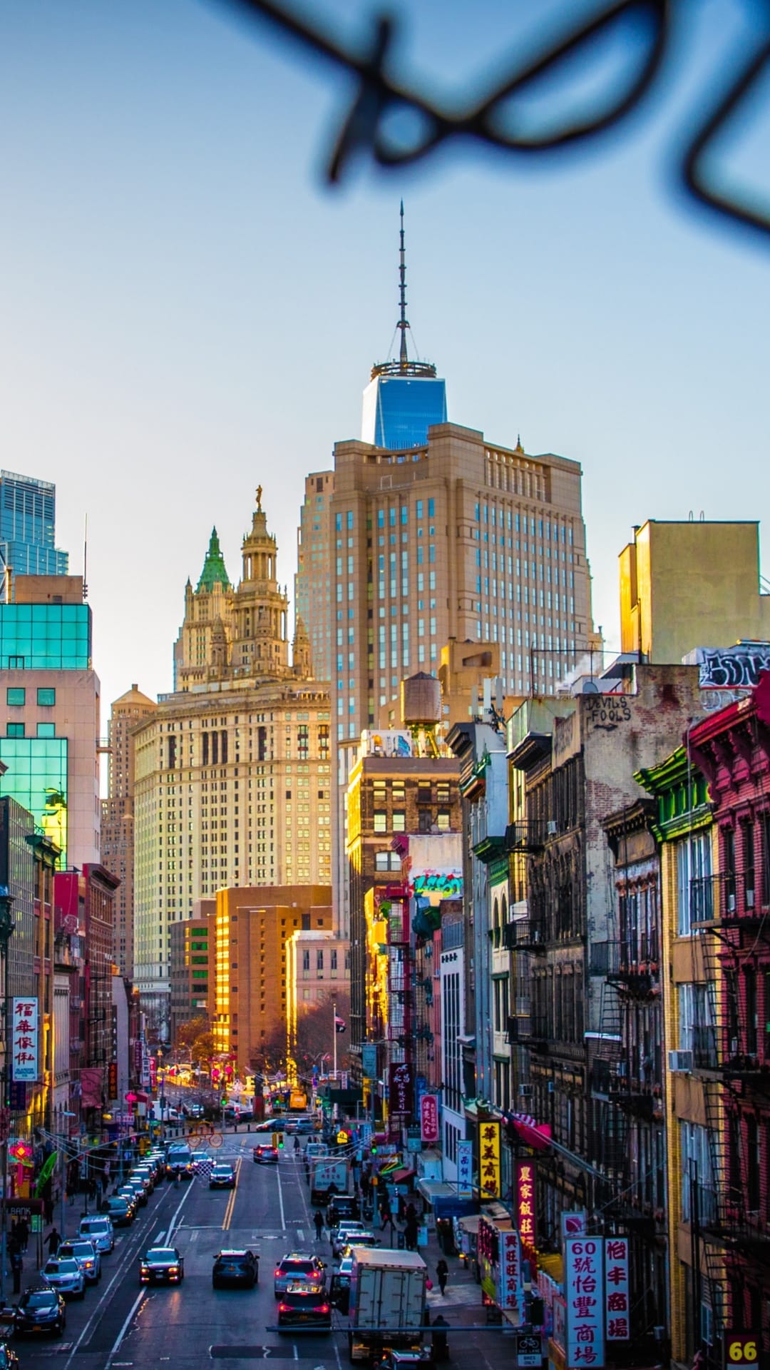 Densely packed historic buildings line a NYC street leading to One World Trade Center under a golden sky.