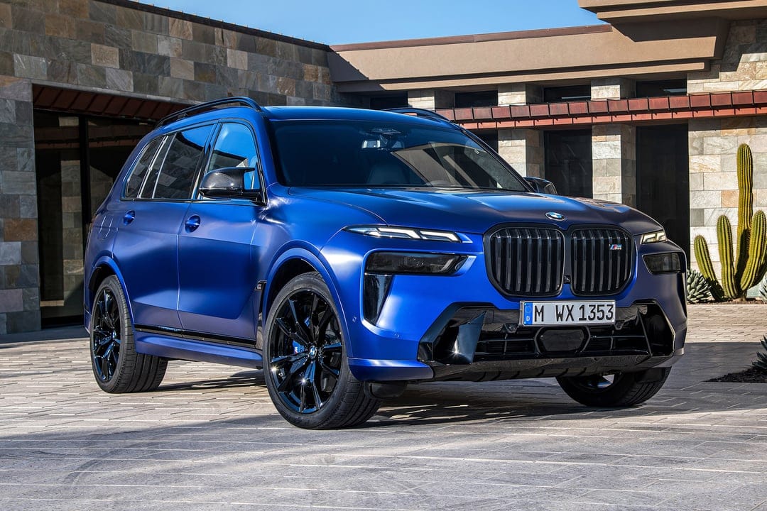 Matte blue BMW X7 SUV with black wheels and grille parked in front of a stone building with a cactus.