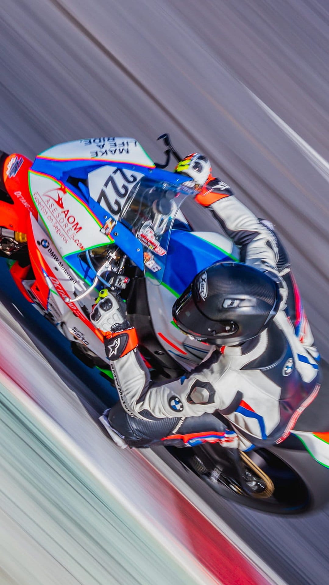 Motorcycle racer in a leather suit leans a sportbike into a sharp turn with motion blur on a gray race track.
