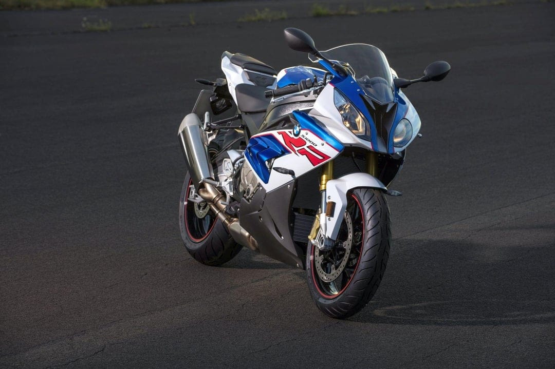 BMW S1000RR motorcycle in white, blue, and red parked on dark asphalt under soft natural lighting.