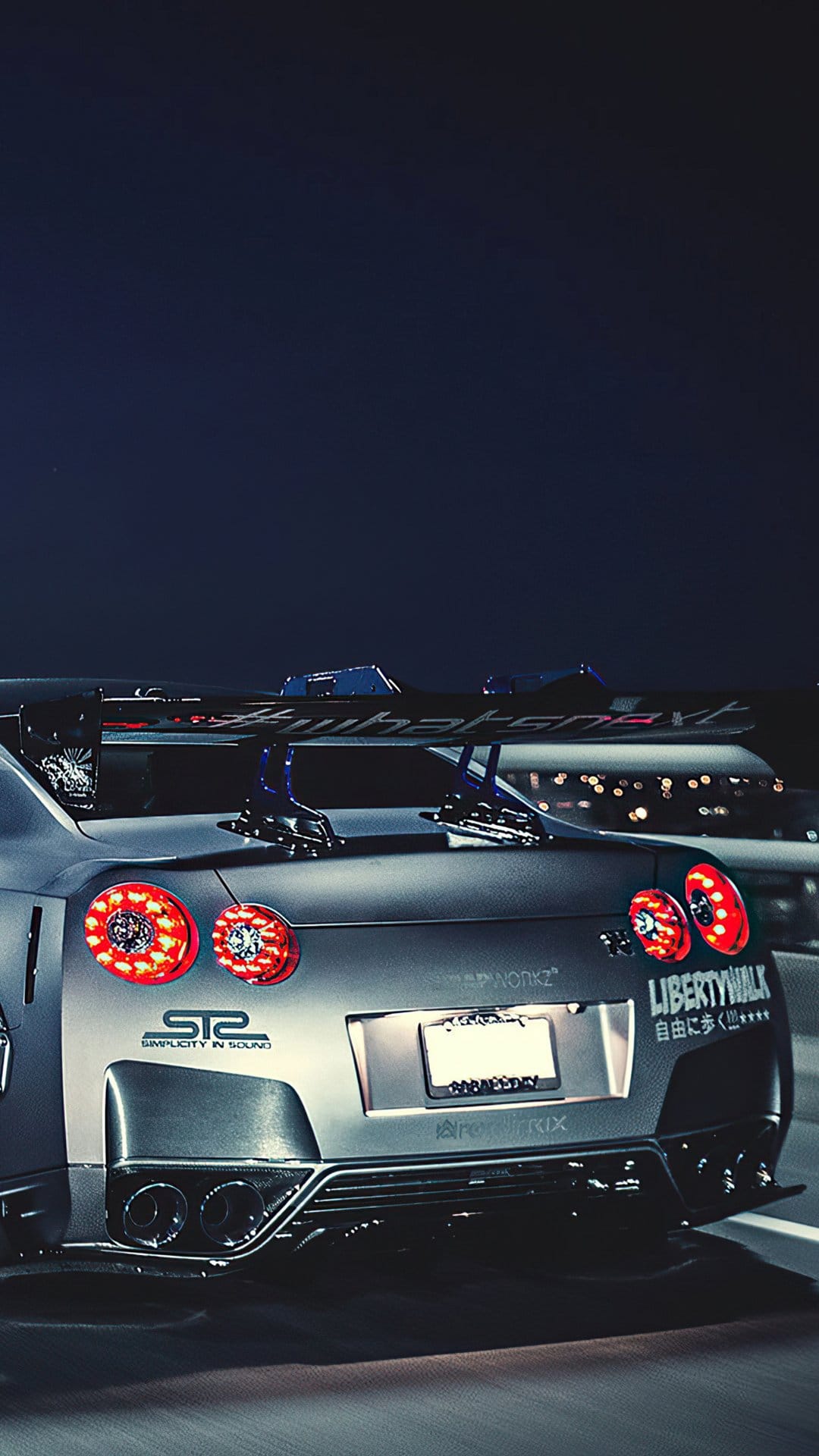 Modified Nissan GT-R rear view featuring glowing red circular taillights and a large wing under a dark night sky.