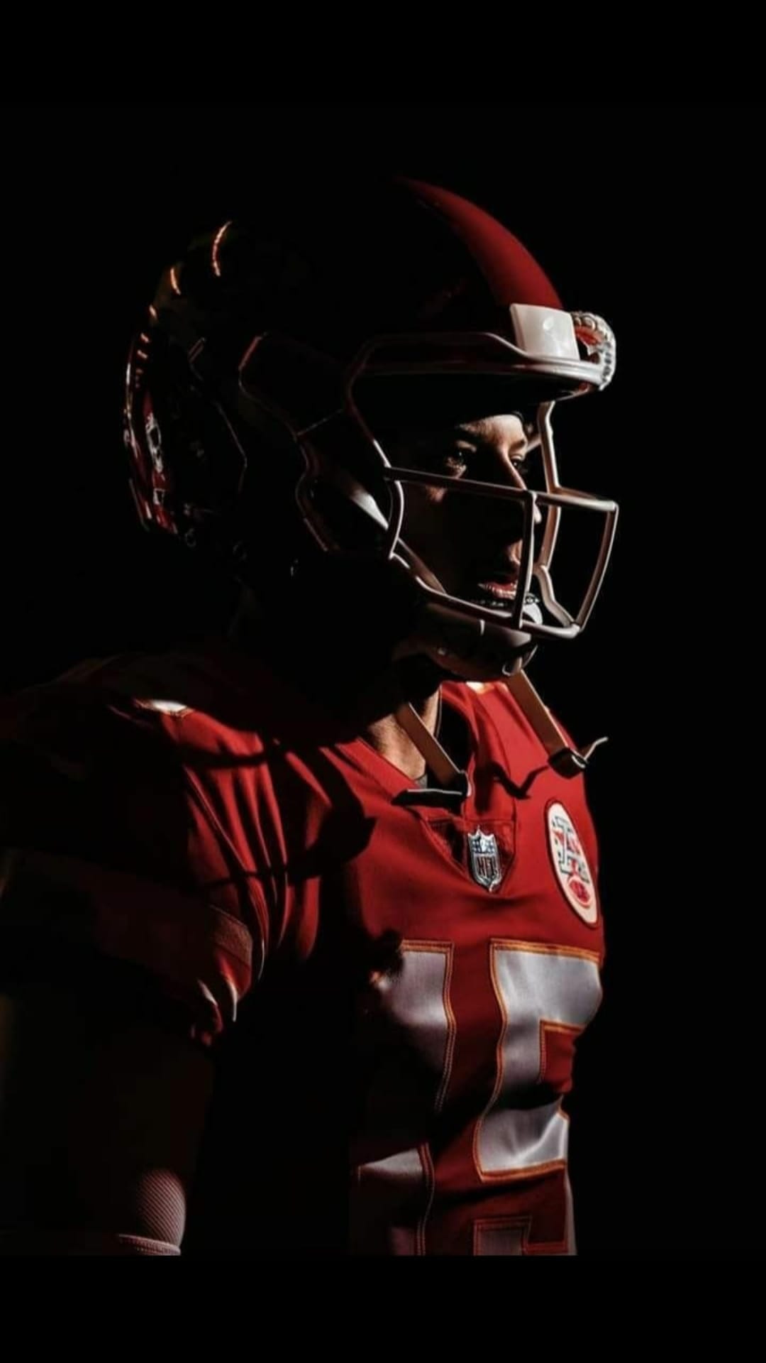Professional football player in a red helmet and jersey poses against a dark background with dramatic side lighting.