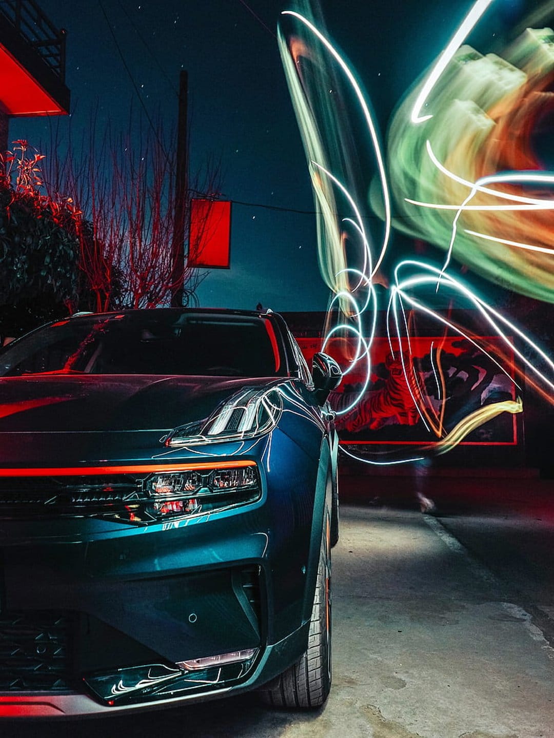 Blue sports car parked at night with green, white, and orange light painting trails circling the chassis.