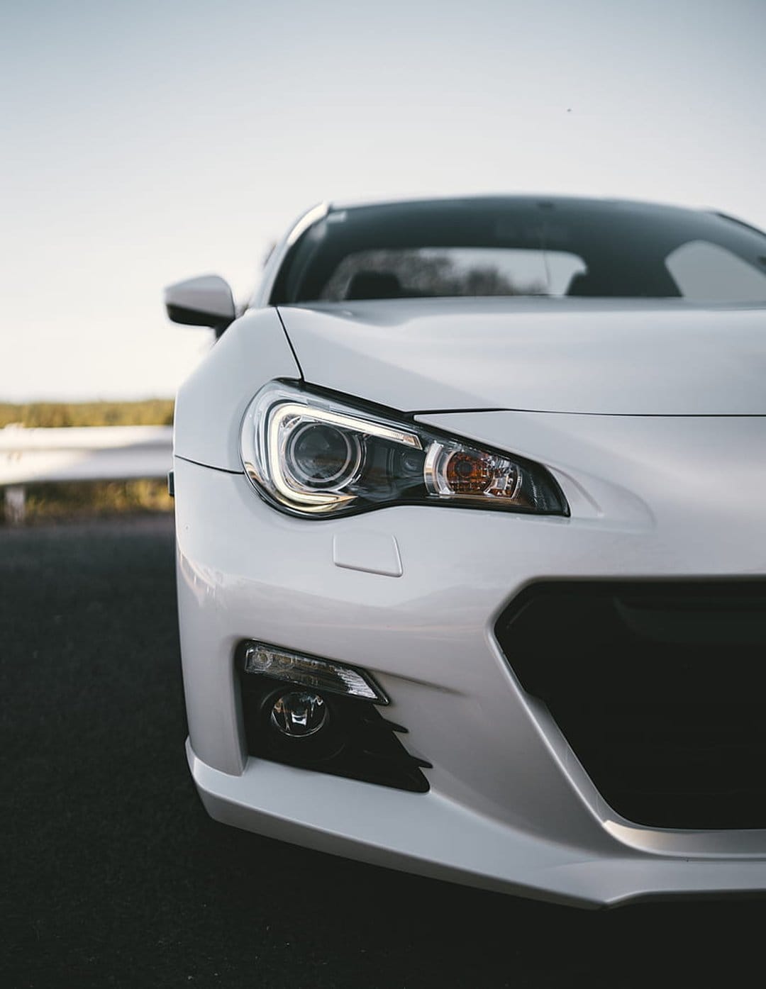White sports car headlight and front grille featuring sharp lines and a dark asphalt ground contrast.
