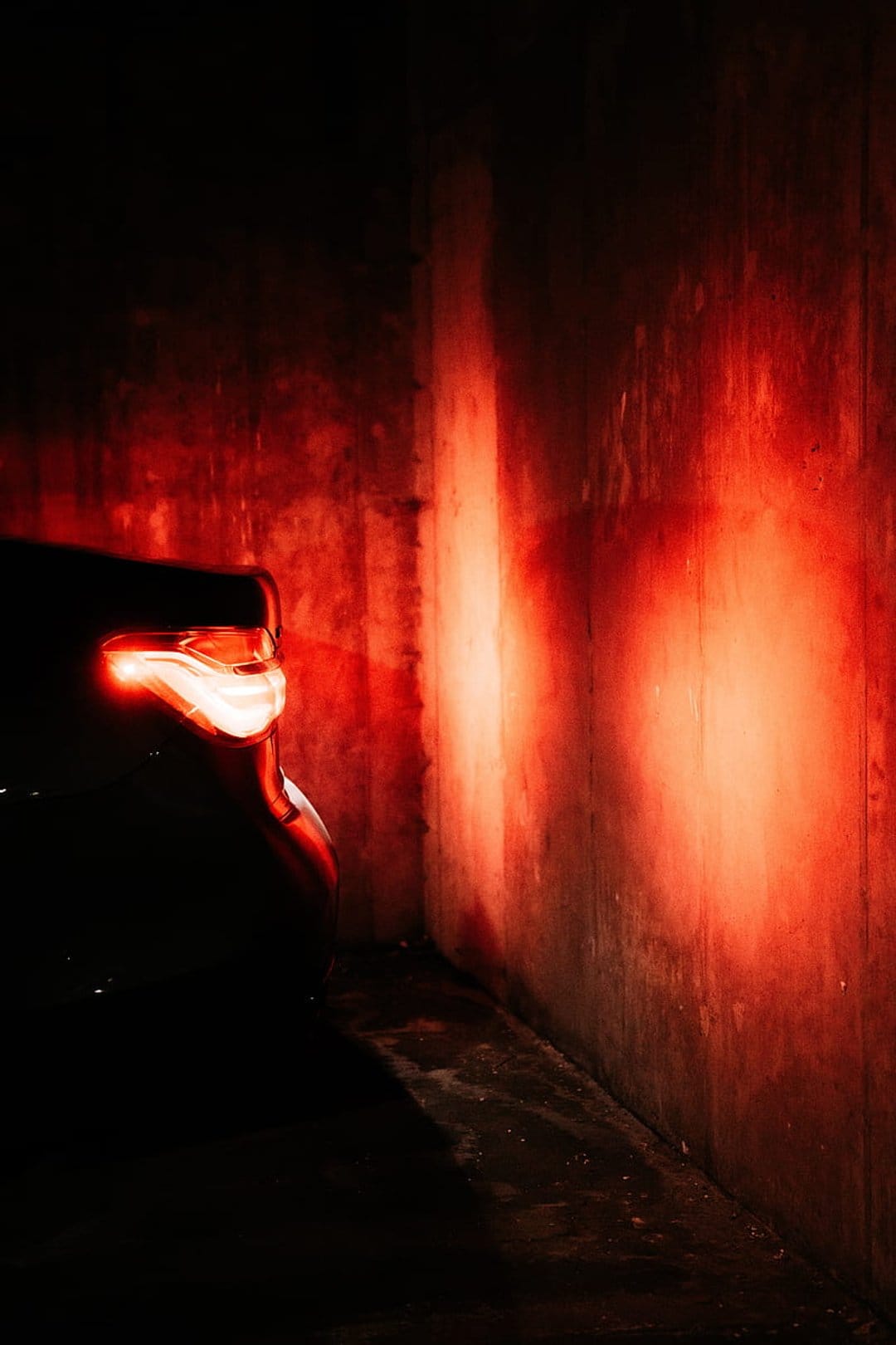 Red car taillight illuminating a gritty concrete alley with a cinematic crimson glow during the night.
