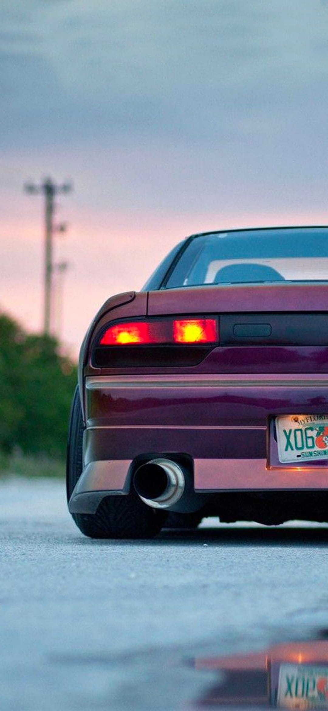 Purple Nissan 240SX S13 rear view featuring glowing taillights and a polished exhaust pipe at sunset.