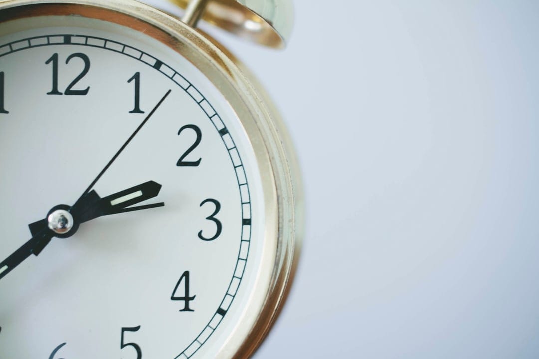 Gold alarm clock face featuring black Arabic numerals and white dial with a soft bokeh background effect.