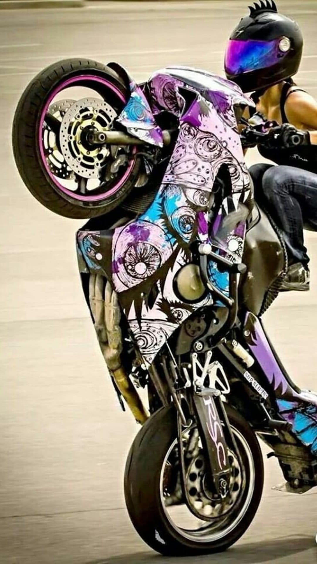 Female rider performs a wheelie on a purple and blue custom sportbike wearing a black helmet with a dark visor.