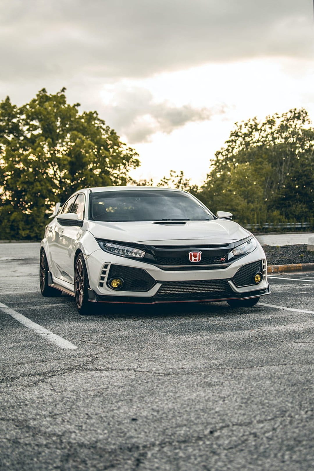 White Honda Civic Type R with a red emblem and black grille parked on asphalt under a cloudy, overcast sky.