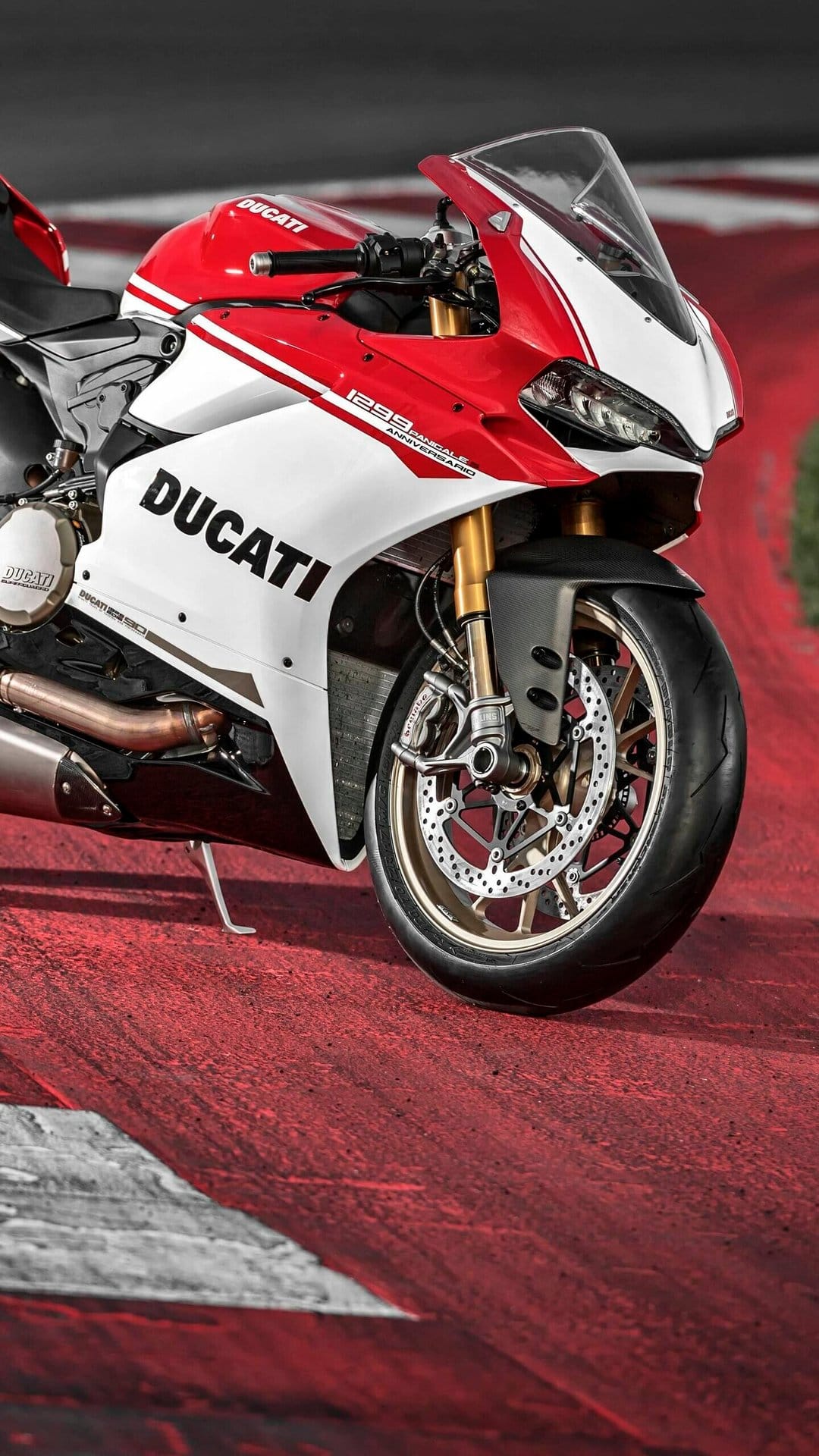 Red and white Ducati 1299 Panigale S Anniversario on a red race track with gold front forks and Brembo brakes.