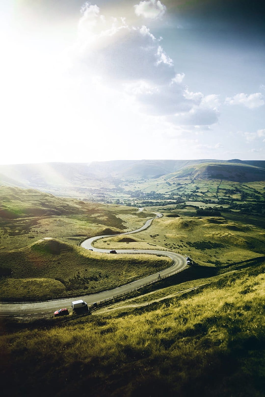 Serpentine asphalt road winding between vibrant green rolling hills with long shadows under bright sunlight.